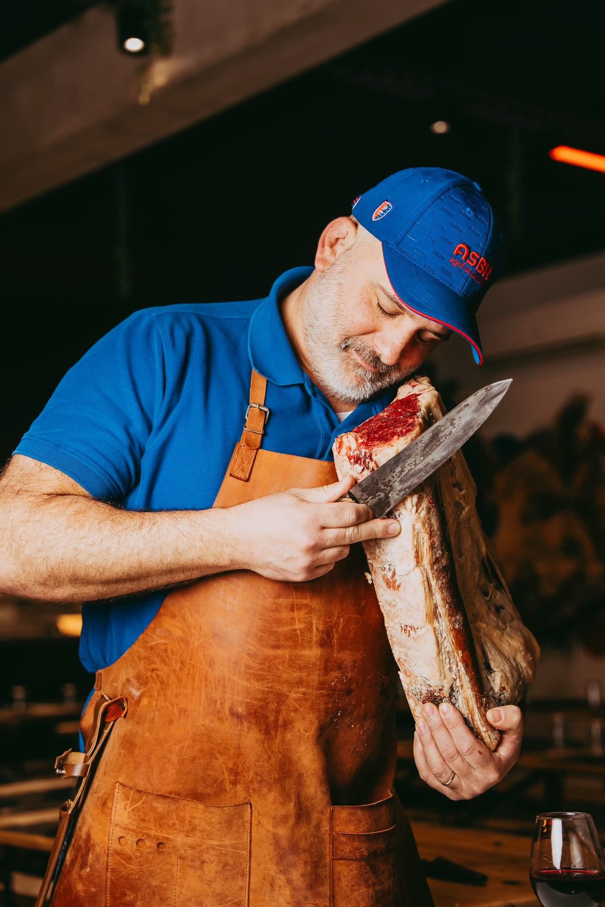 Floréal Vaquerin, casquette ASBH, sent une côte de bœuf maturée dans le clair-obscur du restaurant