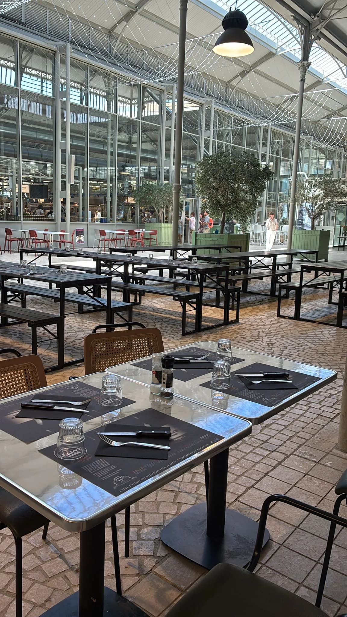 Vue terrasse extérieure sous la halle, oliviers et longues tablées en bois